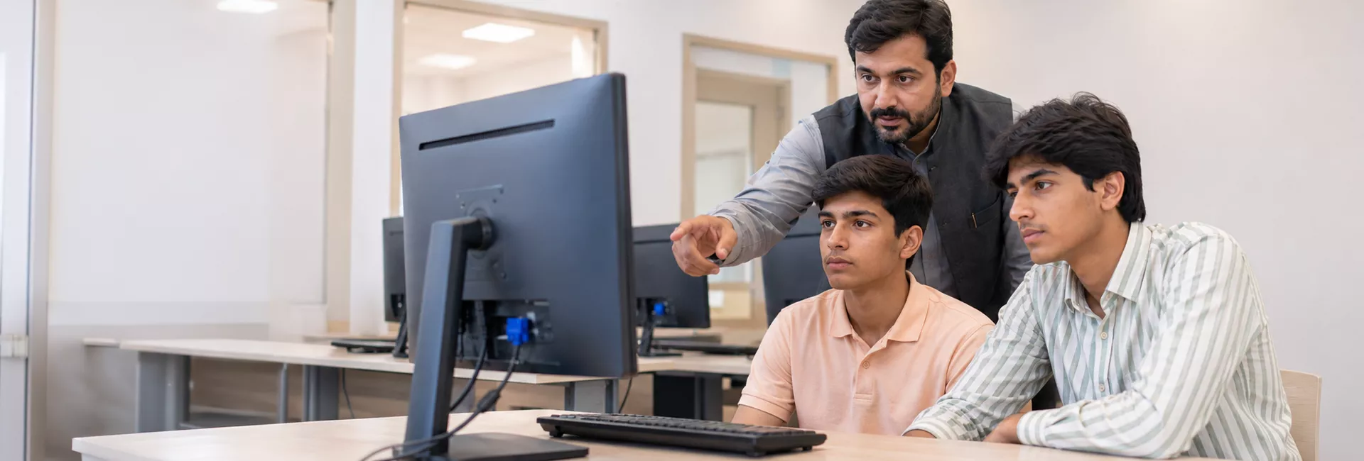 Instructor guiding students at a computer in the SuperTech lab